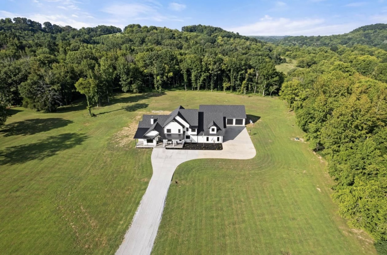 Aerial view of a white farmhouse on open rural land surrounded by woods in Middle Tennessee